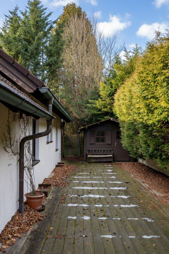 Seitenweg des Hauses mit einem kleinen Gartenhaus und einer dichten Hecke.