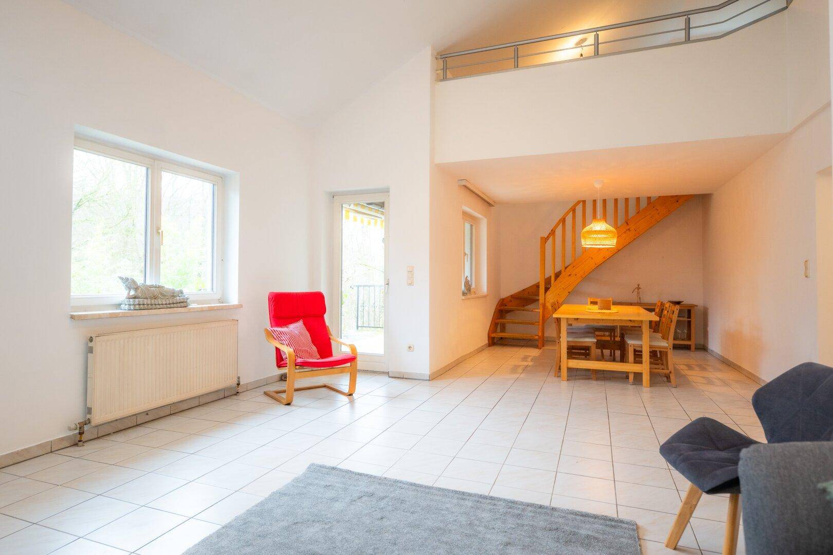 Heller Wohn- und Essbereich mit Fliesenboden, offener Galerie und Zugang zur Terrasse.