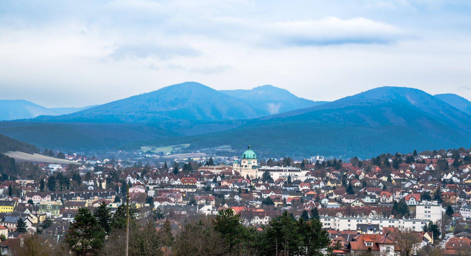Panoramablick auf eine Stadt mit blauen Bergen im Hintergrund unter bewölktem Himmel.