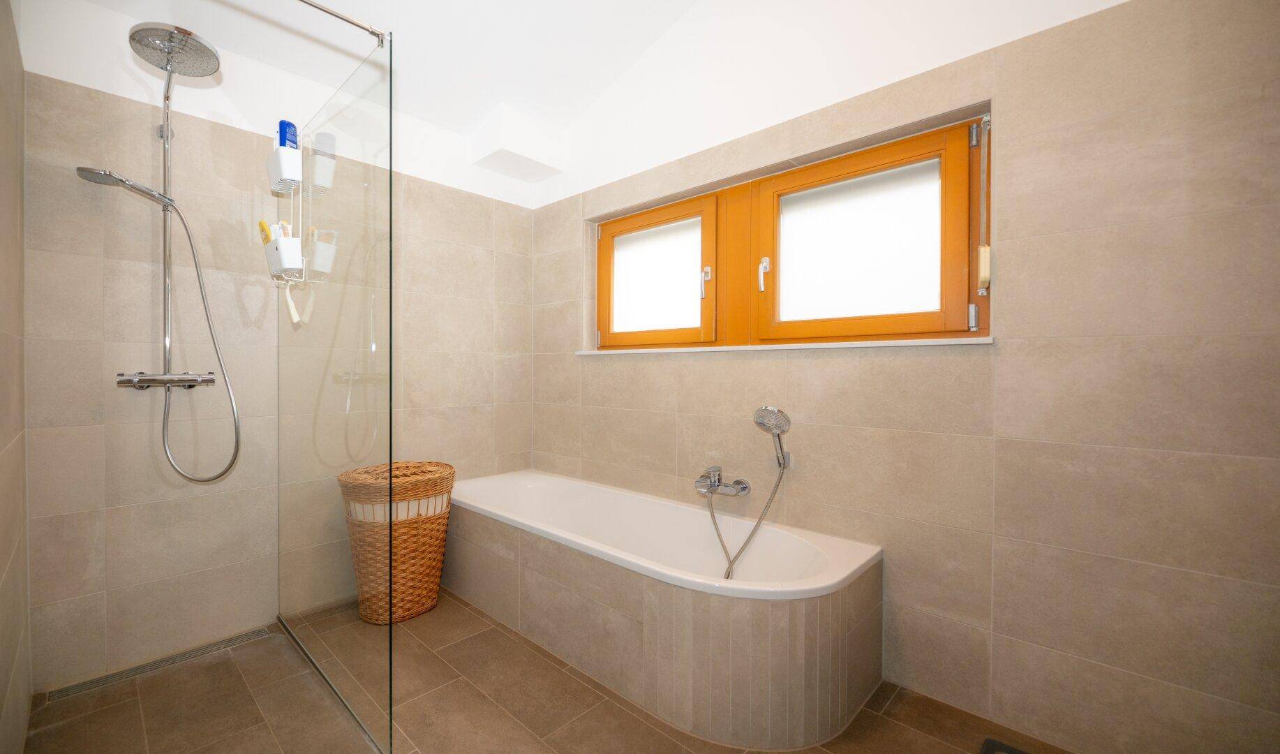 Geräumiges Badezimmer mit Badewanne, Glasdusche und großformatigen Fliesen.