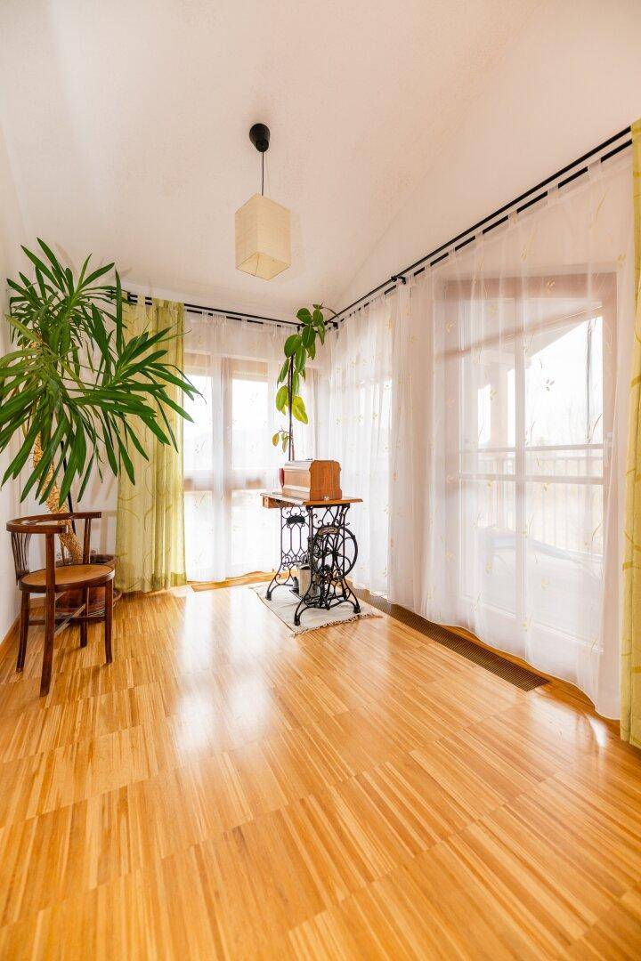Helles Zimmer mit Holzboden und großen Fenstern, die viel Tageslicht hereinlassen.