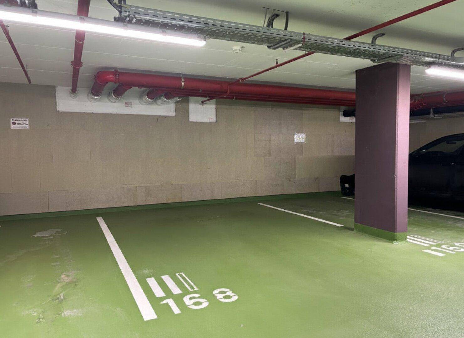 Tiefgaragenstellplatz mit grüner Bodenmarkierung und sichtbaren Installationen an der Decke.
