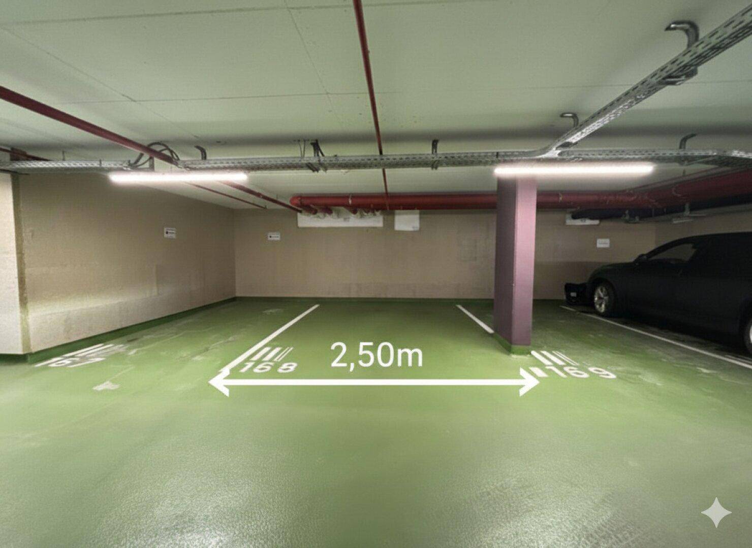 Geräumiger Tiefgaragenstellplatz mit grüner Bodenmarkierung und sichtbaren Deckeninstallationen.