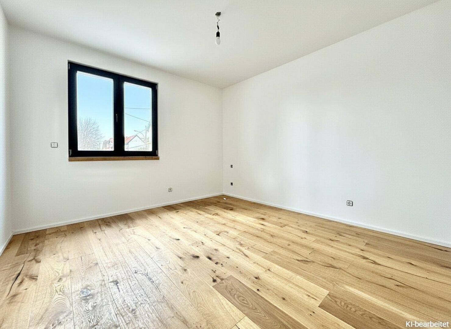 Leeres Schlafzimmer mit hellem Holzparkettboden und einem großen Fenster für viel Tageslicht.