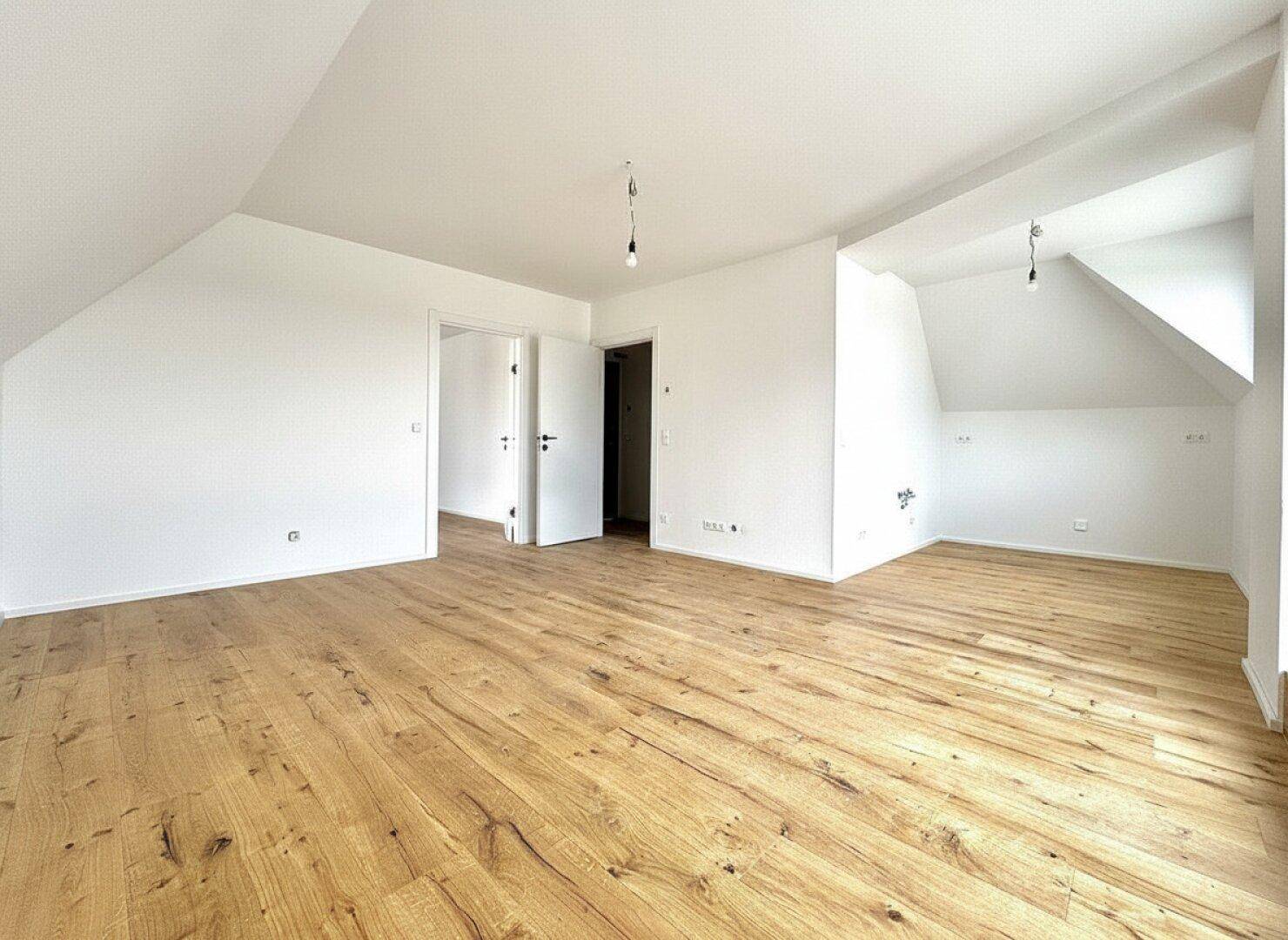 Geräumiger Wohnbereich mit hellem Holzfußboden und weißen Wänden, ideal für individuelle Gestaltung.