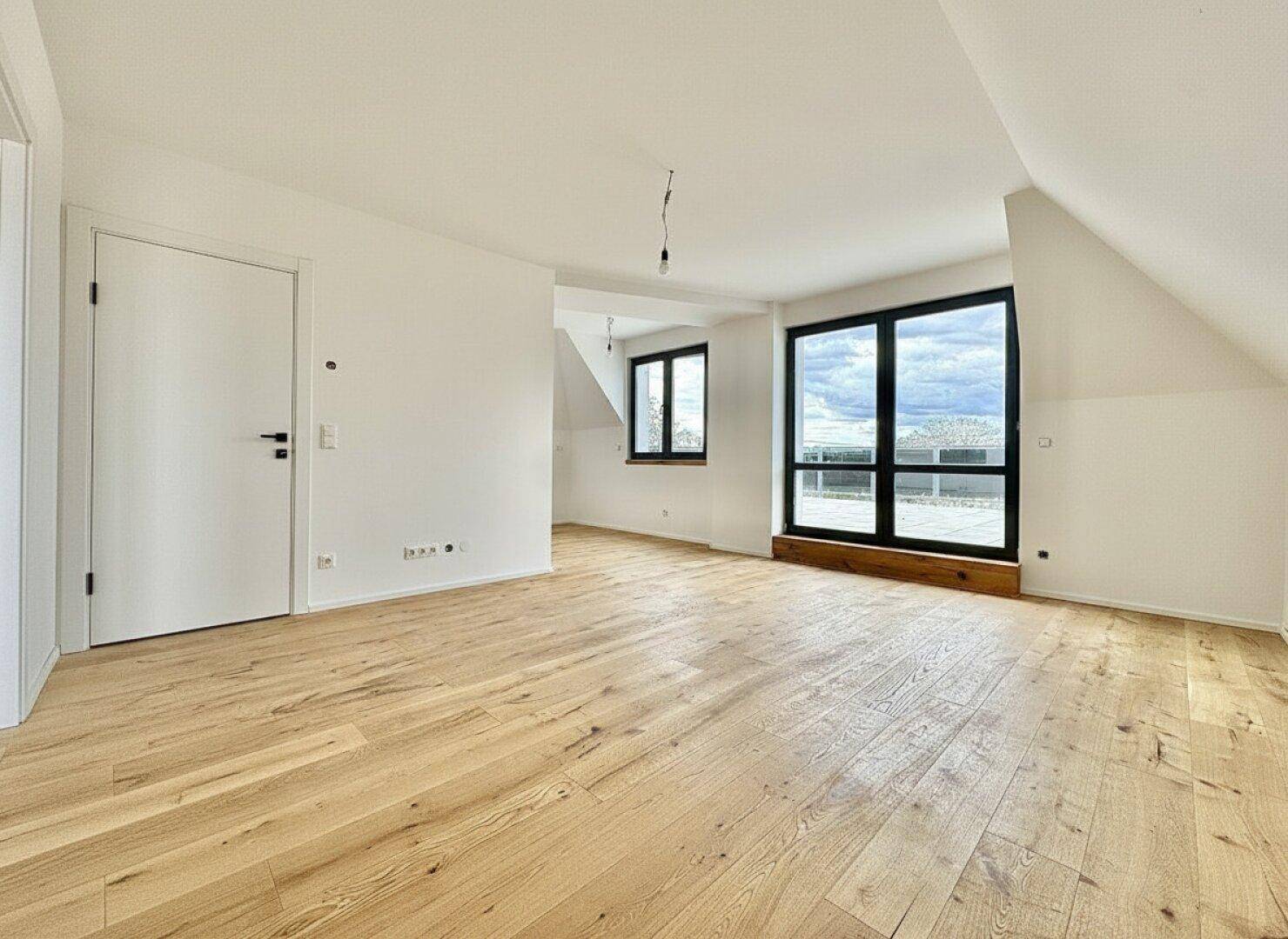 Heller, leerer Raum mit neuem Holzplankenboden, großen Fenstern und Dachschrägen, bereit zum Einzug.