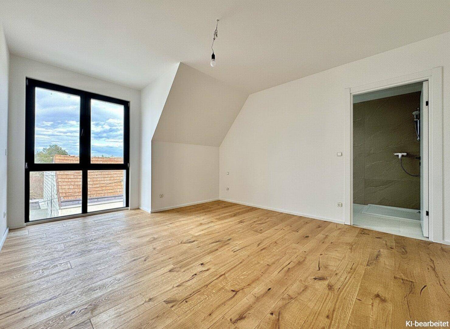 Helles Schlafzimmer mit Holzplankenboden, großen Fenstern und direktem Zugang zu einem Duschbad.