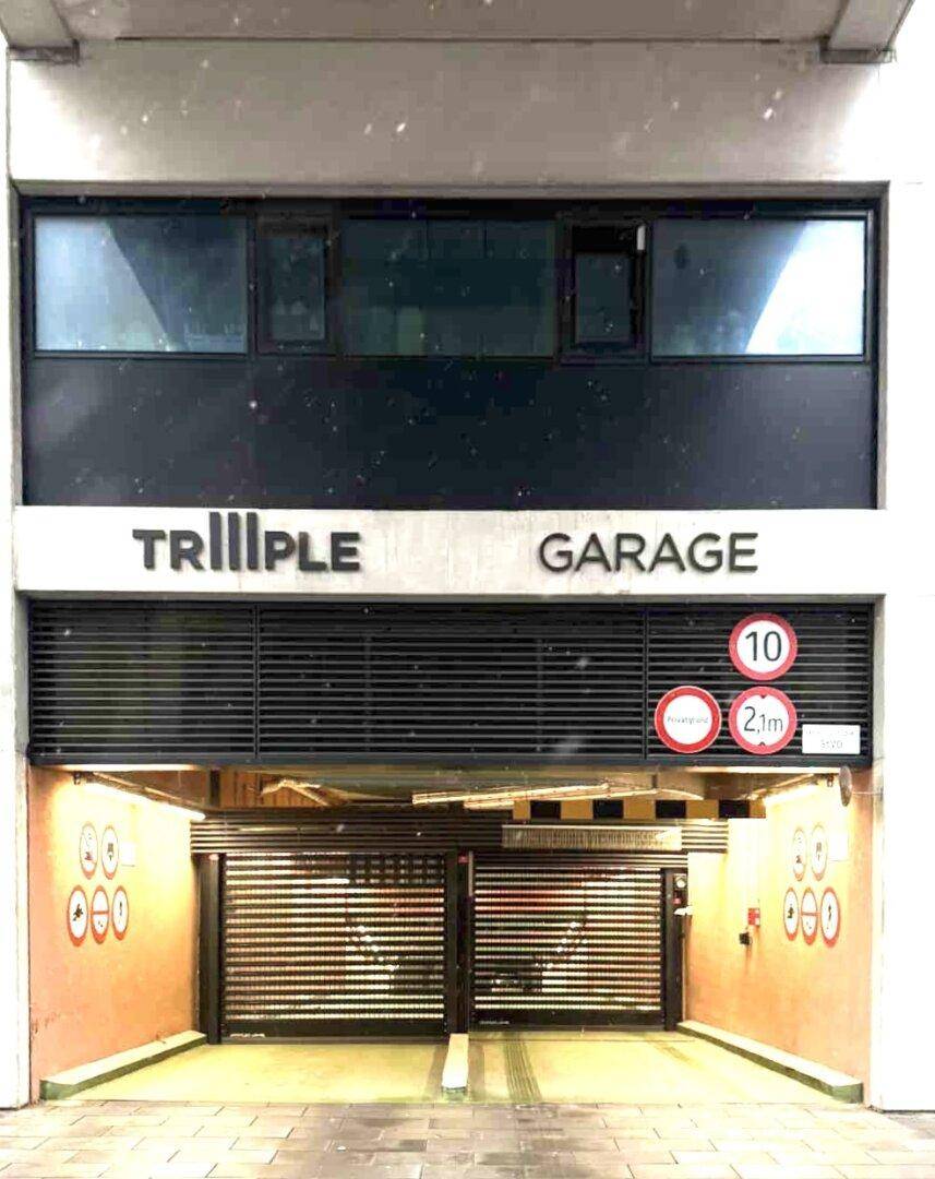 Einfahrt zur Tiefgarage 'TRIIPLE GARAGE' mit geschlossener Schranke und Höhenbegrenzung.