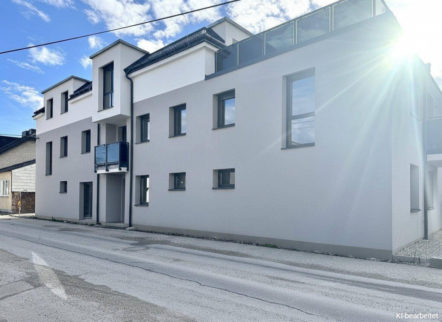 Neubau-Fassade mit großen Fenstern und einem kleinen Balkon bei sonnigem Wetter.
