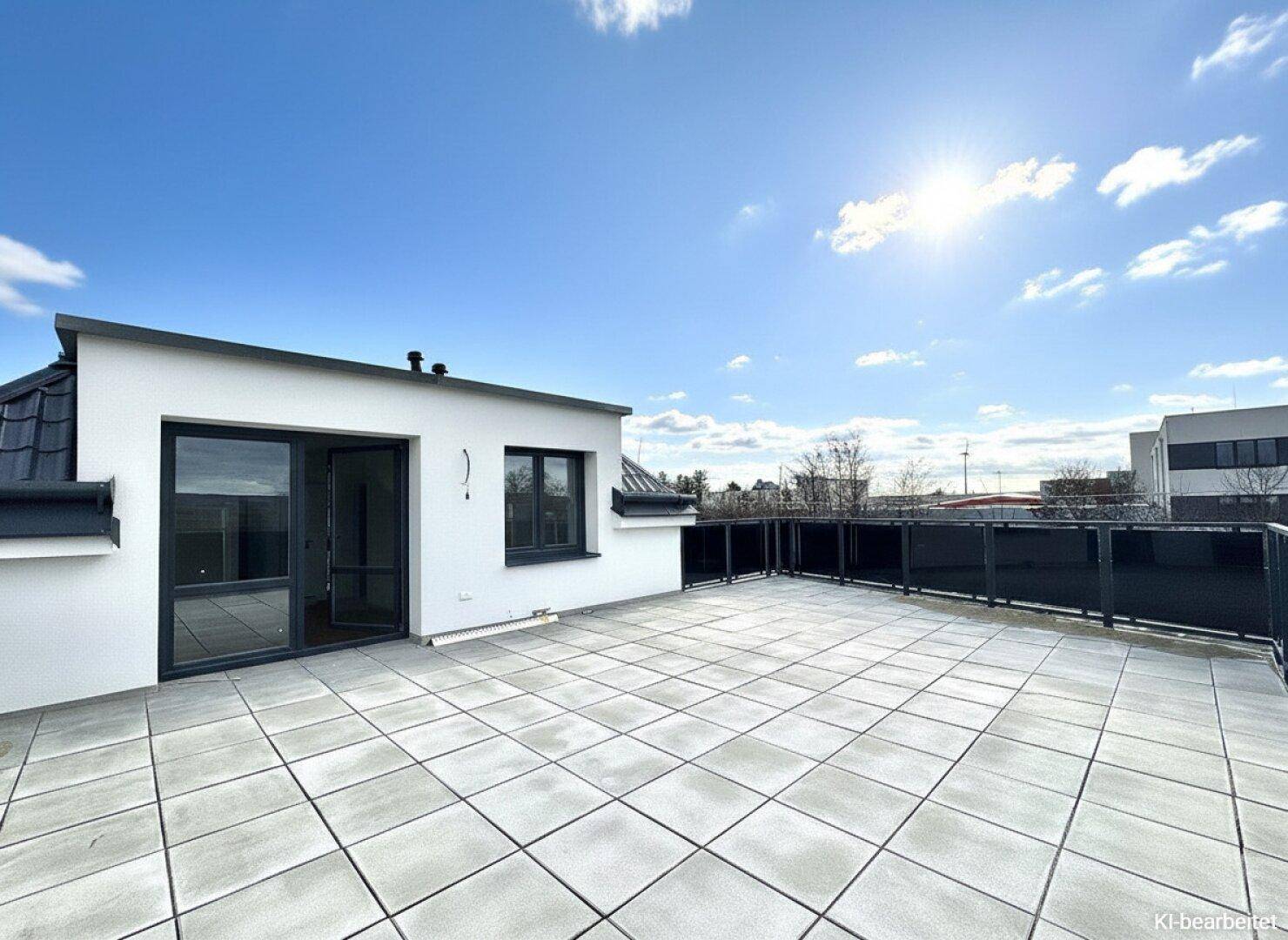 Geräumige Dachterrasse mit hellen Fliesen und schwarzem Geländer unter strahlend blauem Himmel.