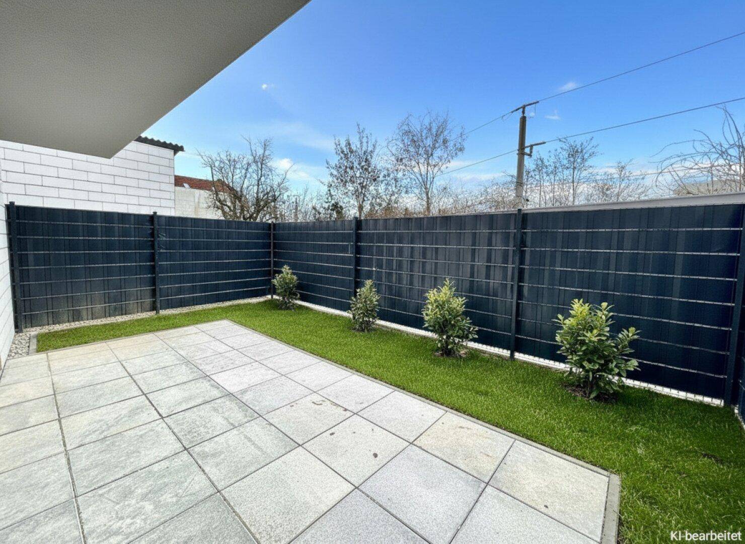 Kleine Terrasse mit Rasenfläche und einem modernen Sichtschutzzaun im Gartenbereich.
