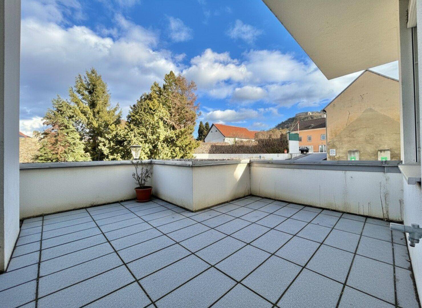 Großer Balkon mit Fliesenboden, umgeben von Bäumen und einem weiten Blick auf die Umgebung.