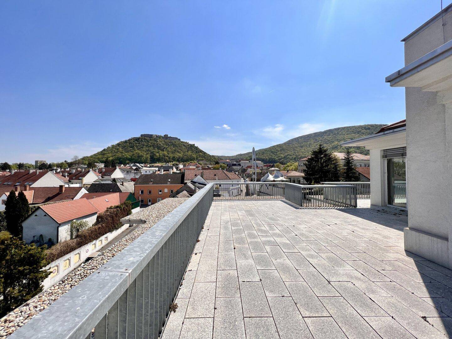 Große Dachterrasse mit Steinplatten und weitem Panoramablick über die Stadt und die grünen Hügel.