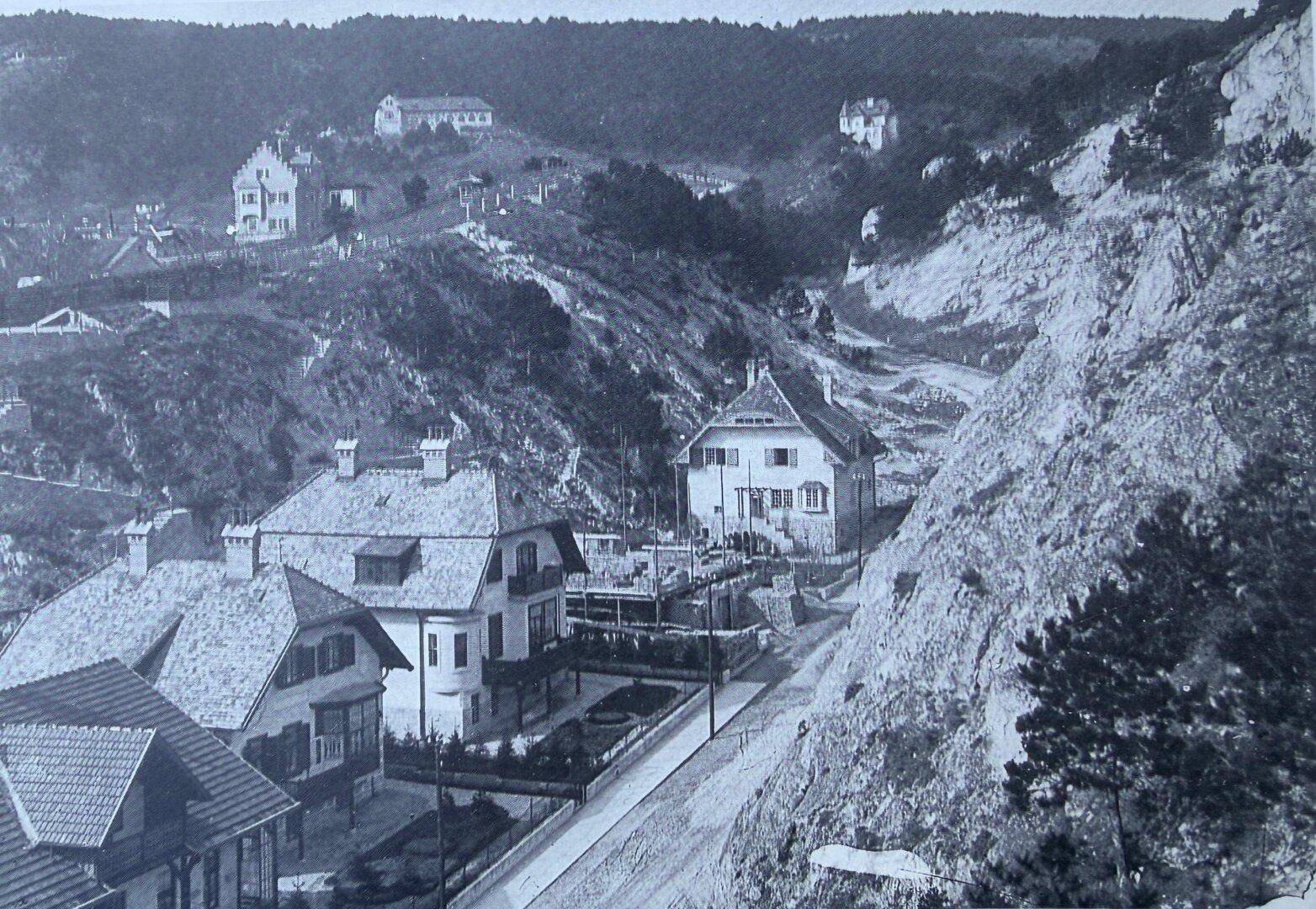 Historische Luftaufnahme einer Siedlung in einer hügeligen, bewaldeten Landschaft.