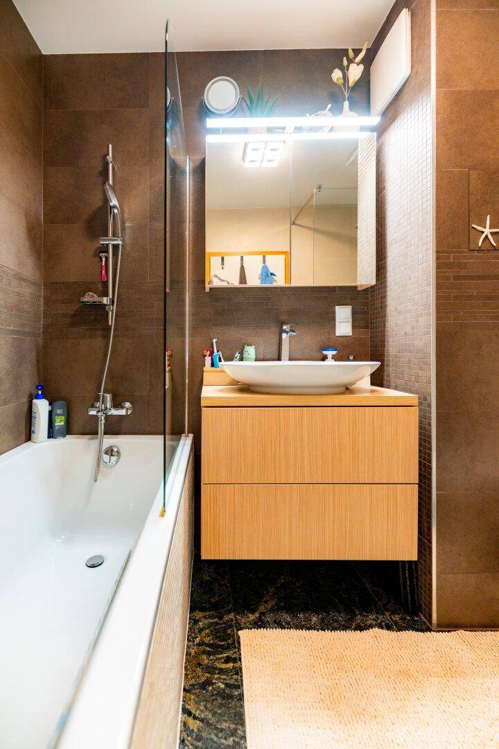 Badezimmer mit Badewanne, Duschabtrennung aus Glas und schwebendem Waschtisch mit Spiegel.