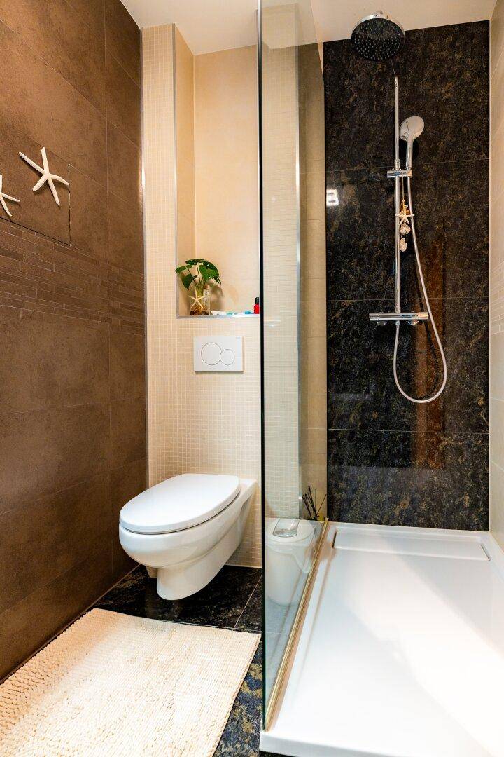 Modernes Badezimmer mit bodengleicher Dusche, Wand-WC und dunklen Fliesen an den Wänden.