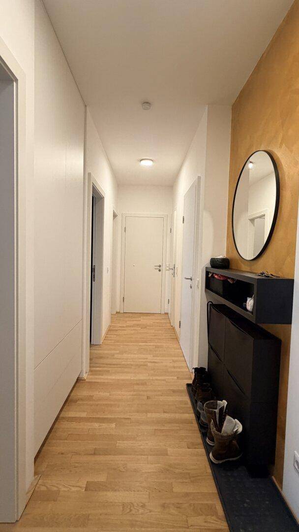 Heller Flur mit Holzboden, Schuhschrank und einem runden Wandspiegel.