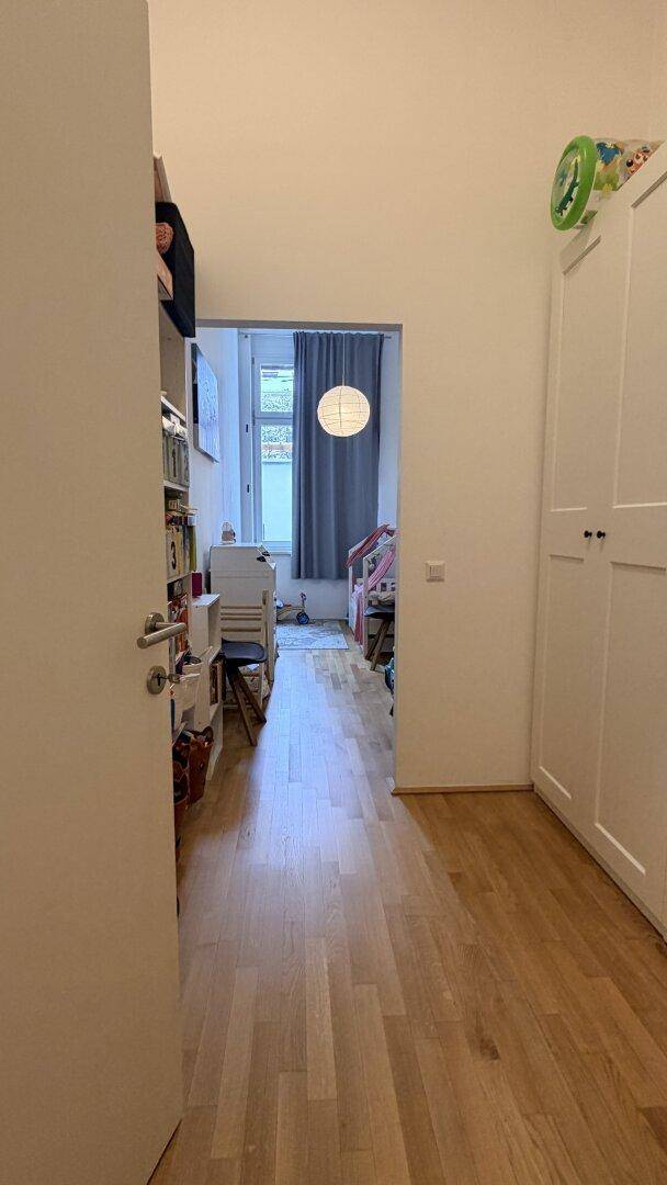Langer Flur mit Holzboden und Blick in ein helles Kinderzimmer mit Fenster.