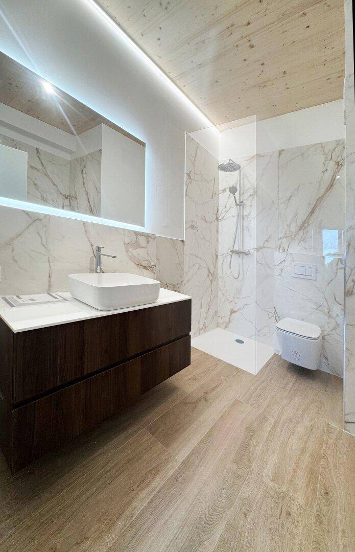Elegantes Badezimmer mit Holzboden, Marmorfliesen und modernem Waschtisch mit Unterschrank.