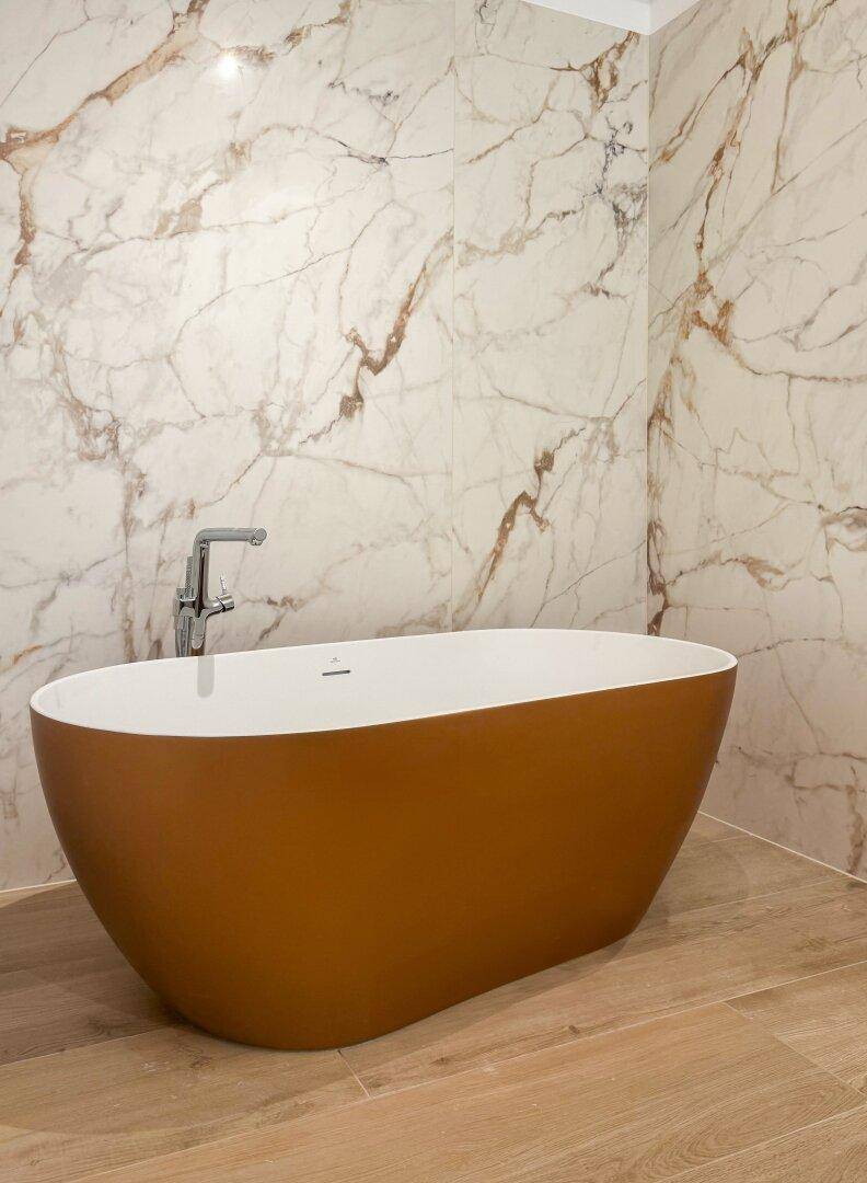 Freistehende Badewanne in einem luxuriösen Badezimmer mit Marmorwand und Holzboden.