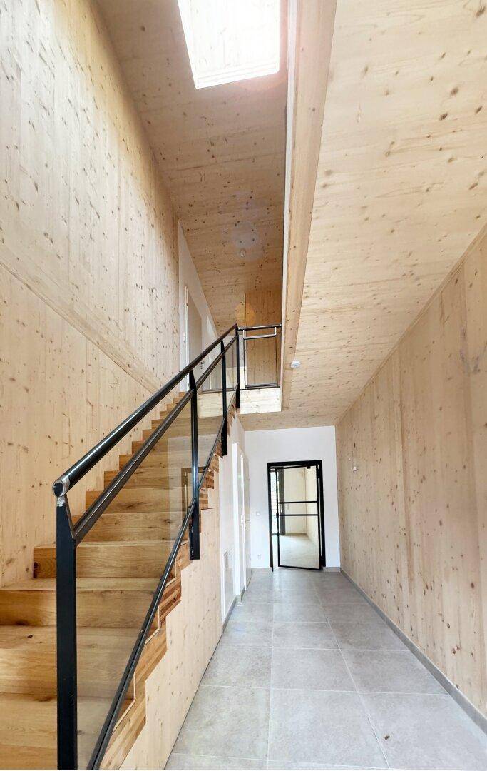Heller Treppenaufgang mit Holzverkleidung, Glasgeländer und Oberlicht für natürliches Licht.