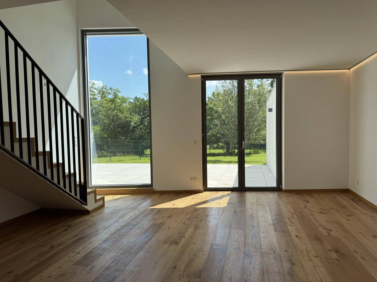 Lichtdurchfluteter Wohnbereich mit Echtholzparkett, moderner Treppe und Zugang zur Terrasse mit Gartenblick.