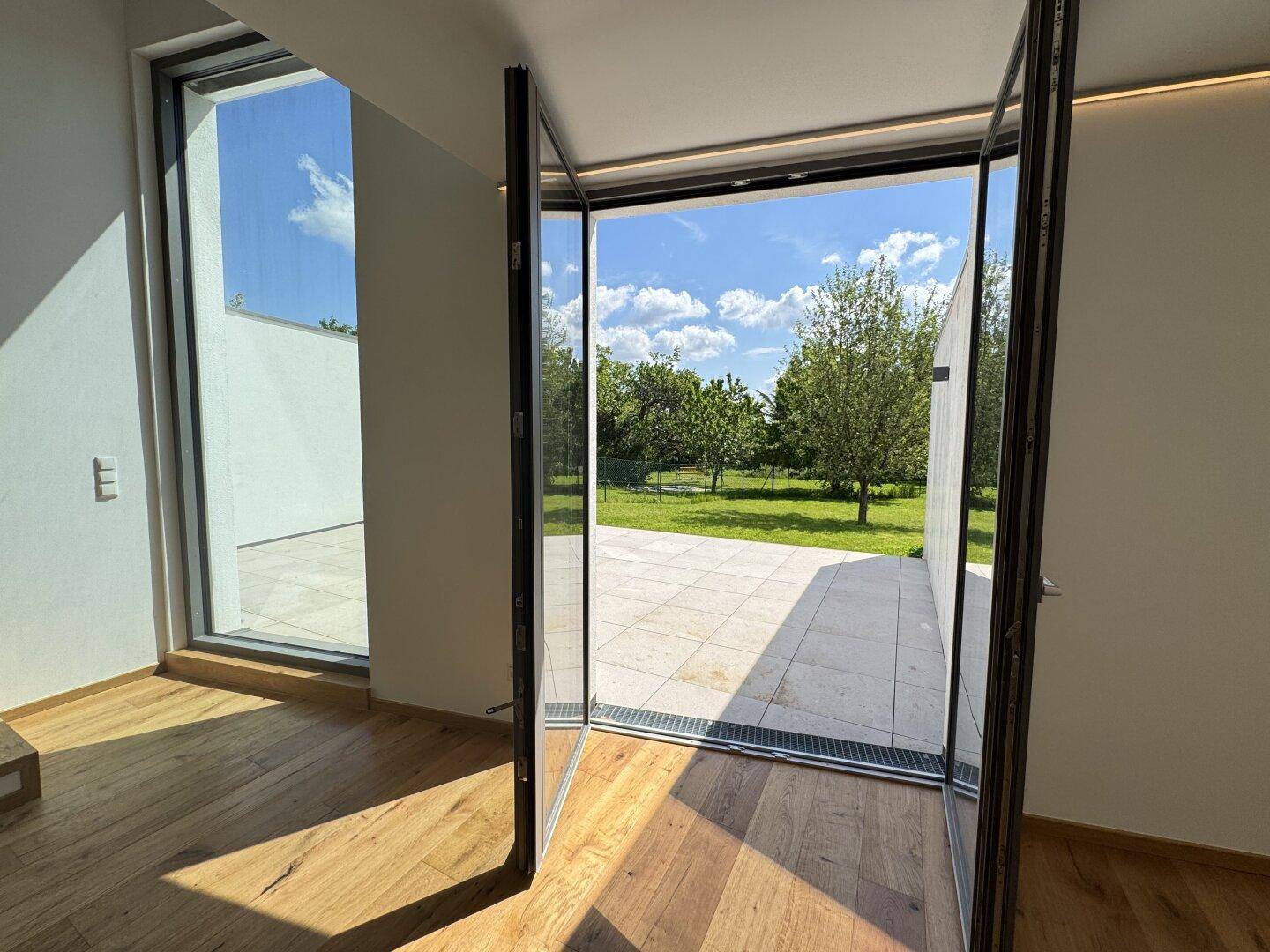 Große Glasflügeltüren öffnen sich zu einer sonnigen Terrasse und dem weitläufigen Garten.