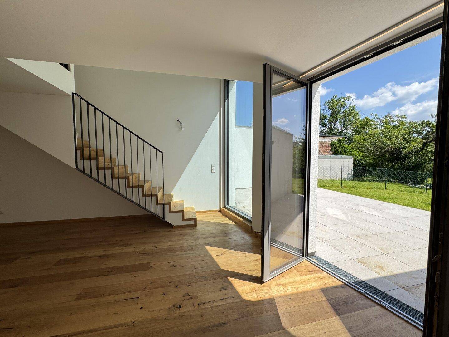 Heller Wohnbereich mit moderner Treppe und direktem Zugang zur Außenterrasse und dem Garten.