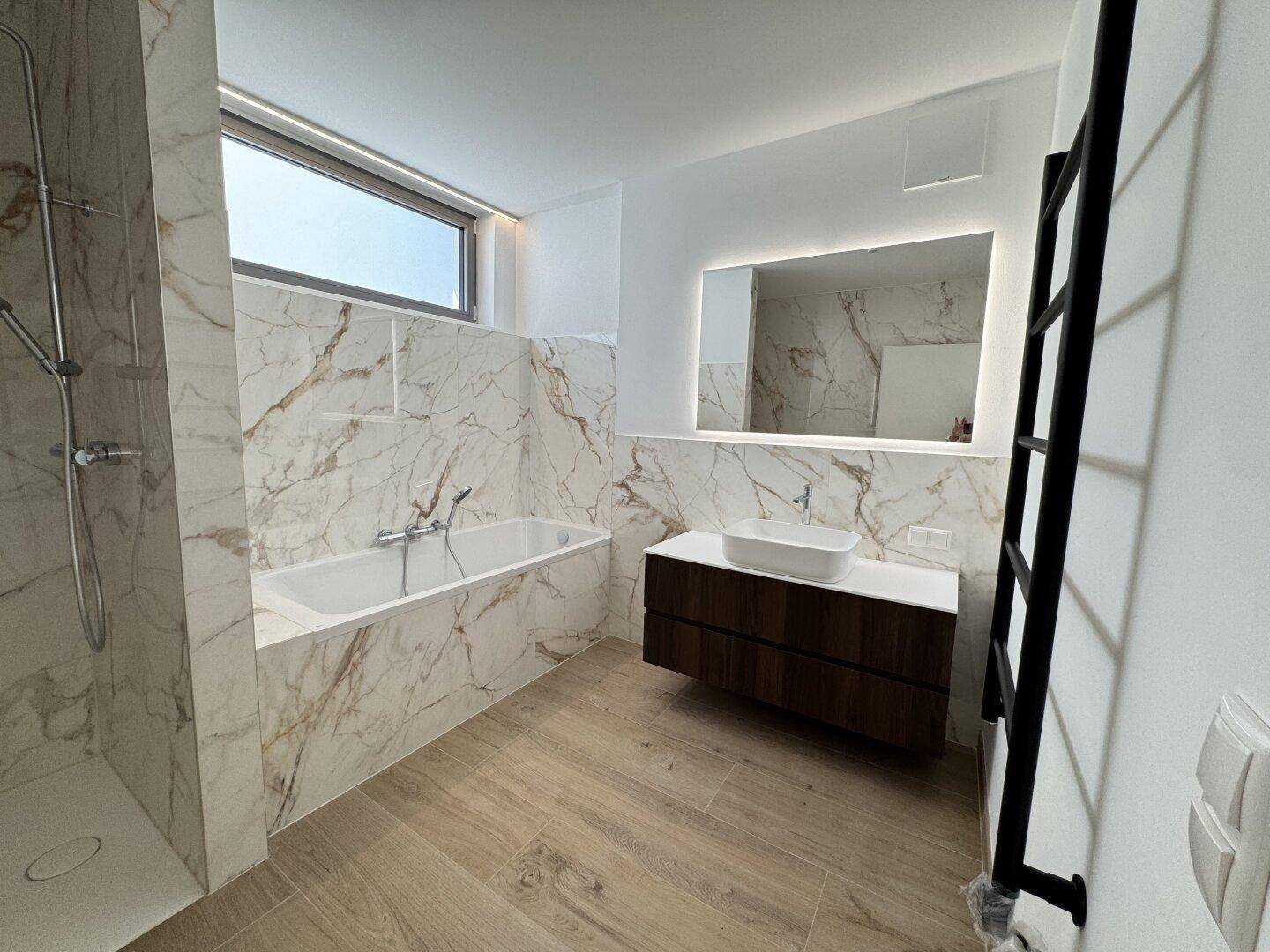 Modernes Badezimmer mit Marmoroptik-Fliesen, Badewanne, ebenerdiger Dusche und großem Fenster.
