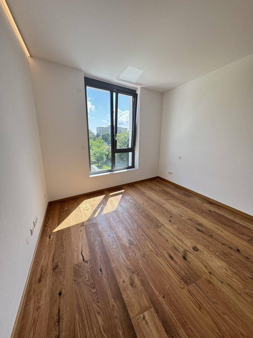 Geräumiges Schlafzimmer mit Holzboden und großem Fenster mit Blick ins Grüne.