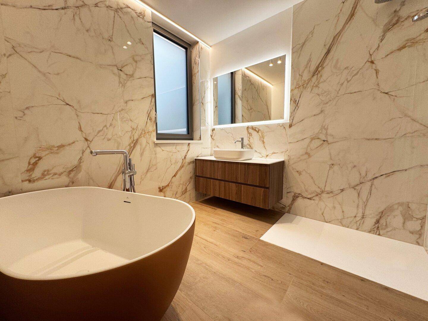 Modernes Badezimmer mit freistehender Badewanne, Marmorfliesen und schwebendem Waschtisch.