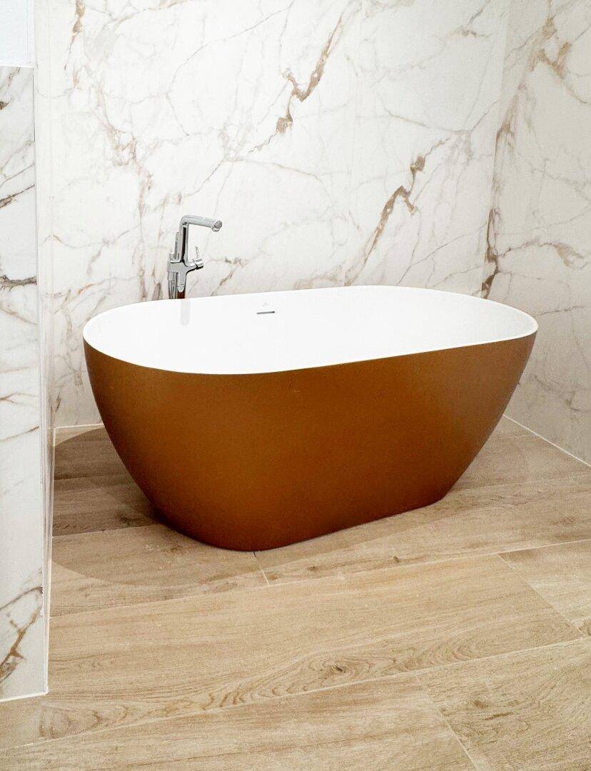 Nahaufnahme einer eleganten, freistehenden Badewanne vor einer Wand mit Marmorfliesen.
