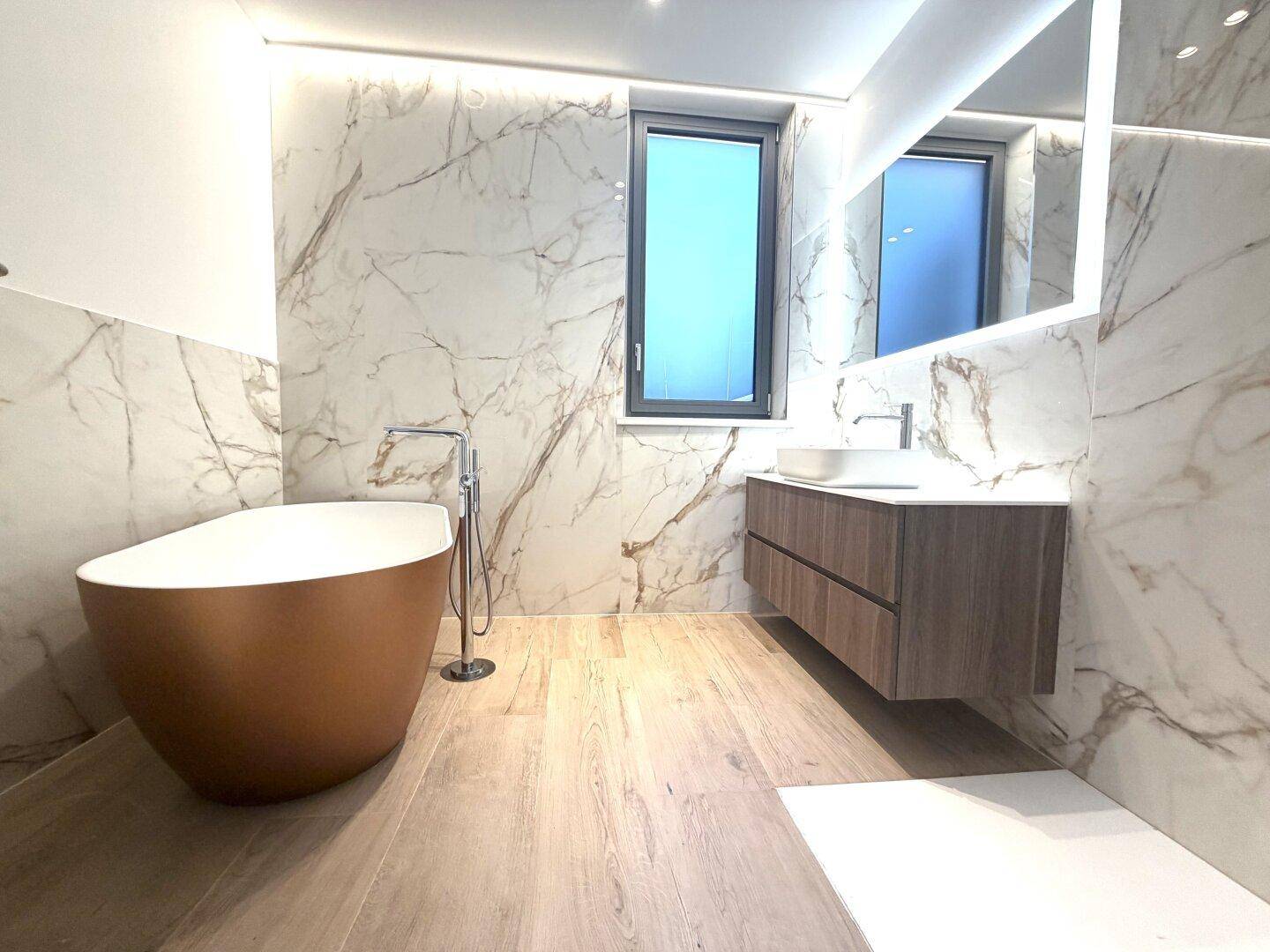 Elegantes Badezimmer mit freistehender Badewanne, Marmorfliesen und modernem Waschtisch.