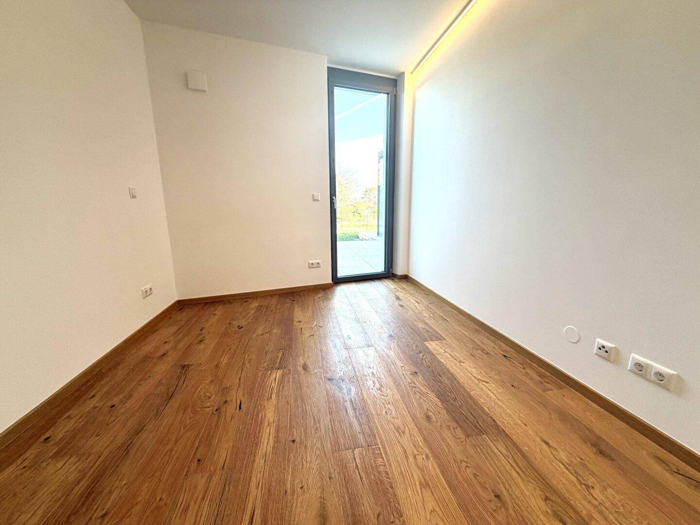 Heller, leerer Raum mit Holzboden und Zugang zu einem Außenbereich.