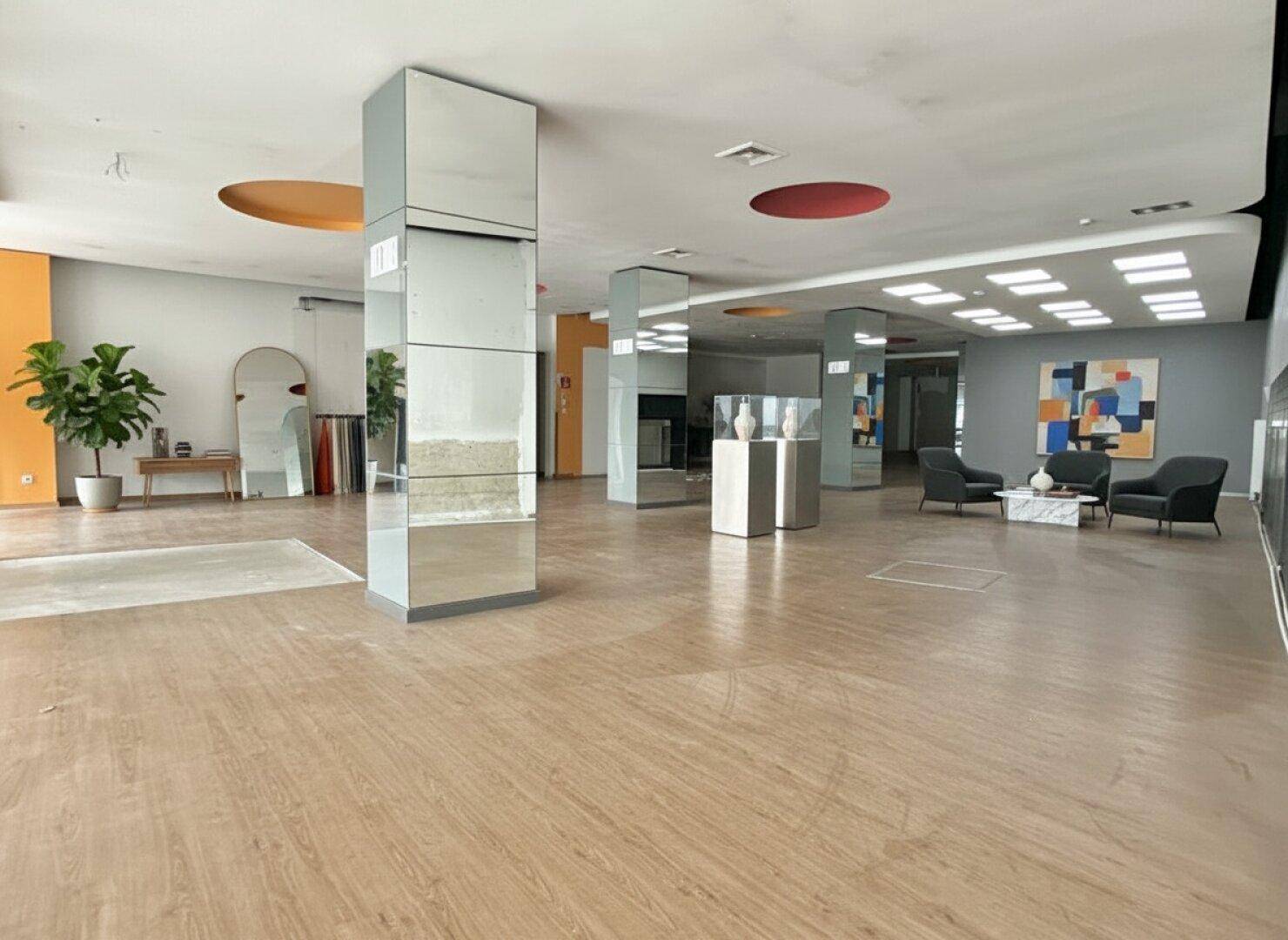 Großer, offener Gewerberaum mit hellem Holzboden, hohen Decken und modernen Spiegelsäulen.