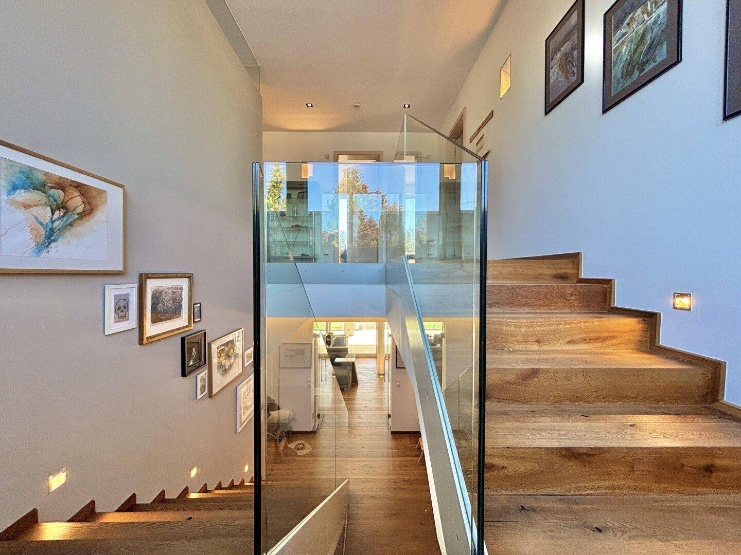 Elegantes Treppenhaus mit Holzstufen und moderner Glasbrüstung, das die Etagen verbindet.
