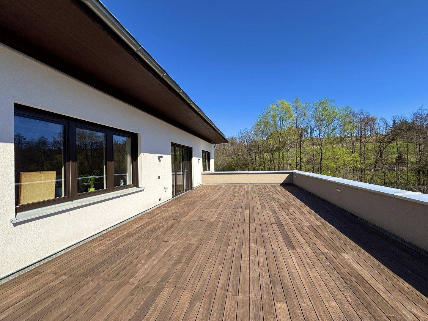 Weitläufige Dachterrasse mit Holzboden und weitem Blick auf die grüne Umgebung.