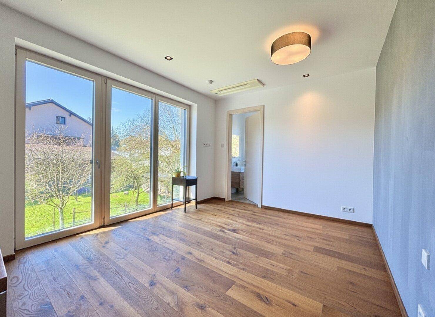 Geräumiges Schlafzimmer mit Holzboden und großen Fenstern, die viel Tageslicht hereinlassen.