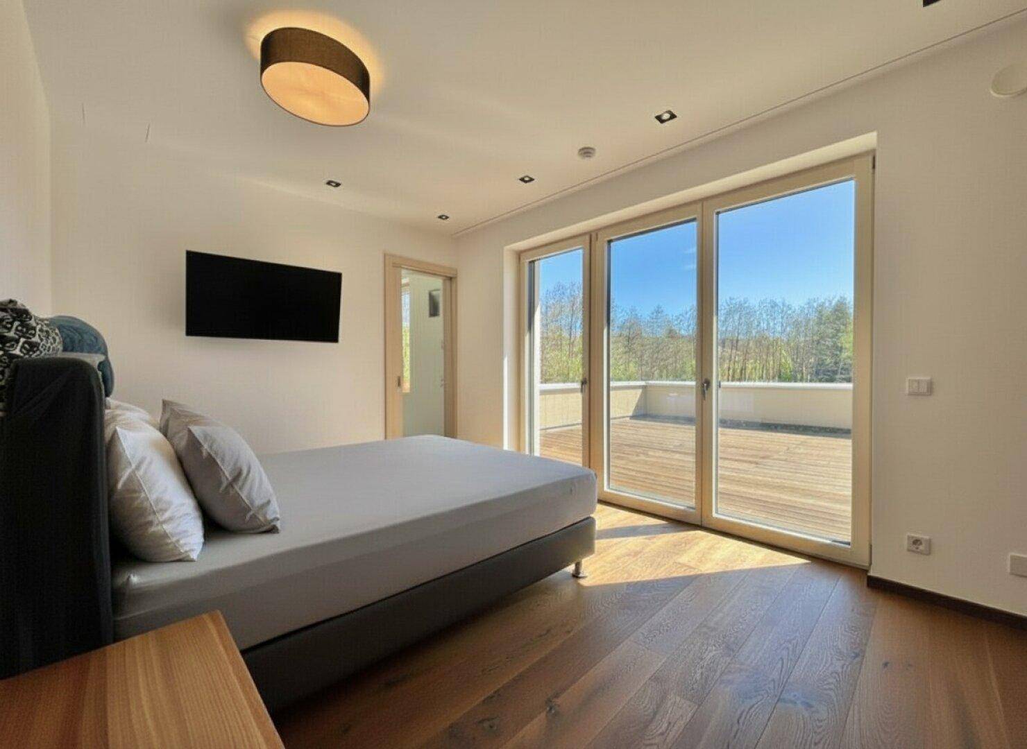 Helles Schlafzimmer mit Bett, Holzboden und direktem Zugang zu einer großen Dachterrasse.