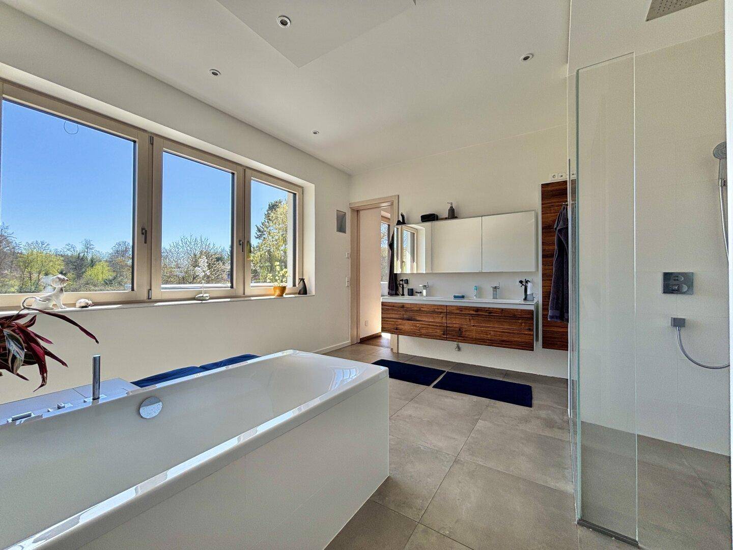 Modernes Badezimmer mit freistehender Badewanne, begehbarer Dusche und großen Fenstern.