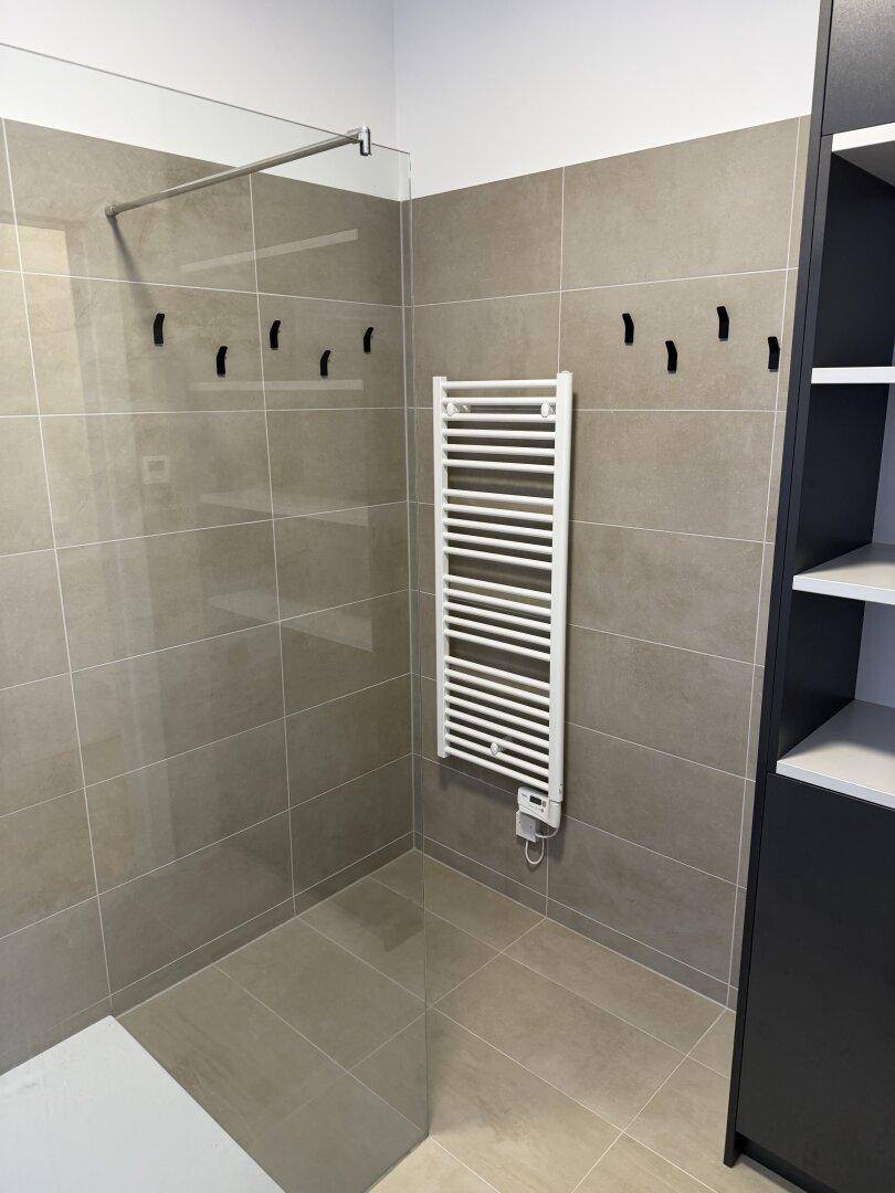 Ebenerdige Dusche in einem modernen Badezimmer mit großformatigen Fliesen und Handtuchheizkörper.