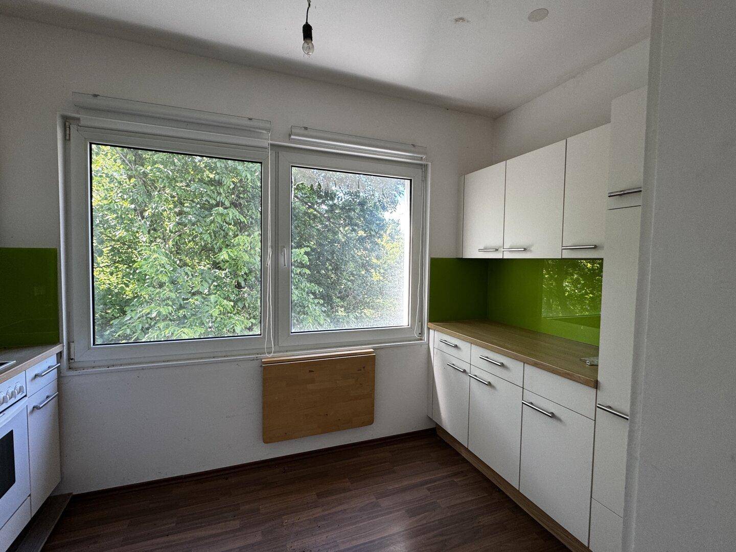 Moderne Küche mit weißen Schränken, Holztheke und grünem Spritzschutz, Blick ins Grüne.