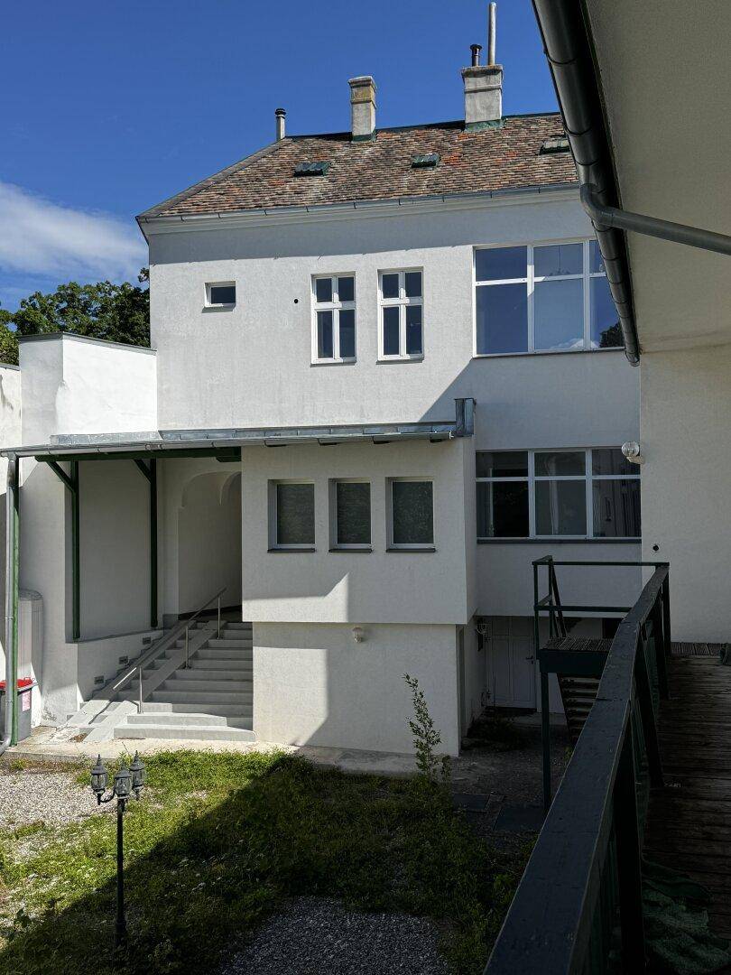 Detailansicht der weißen Gebäudefassade mit Außentreppe und einem kleinen Rasenbereich.