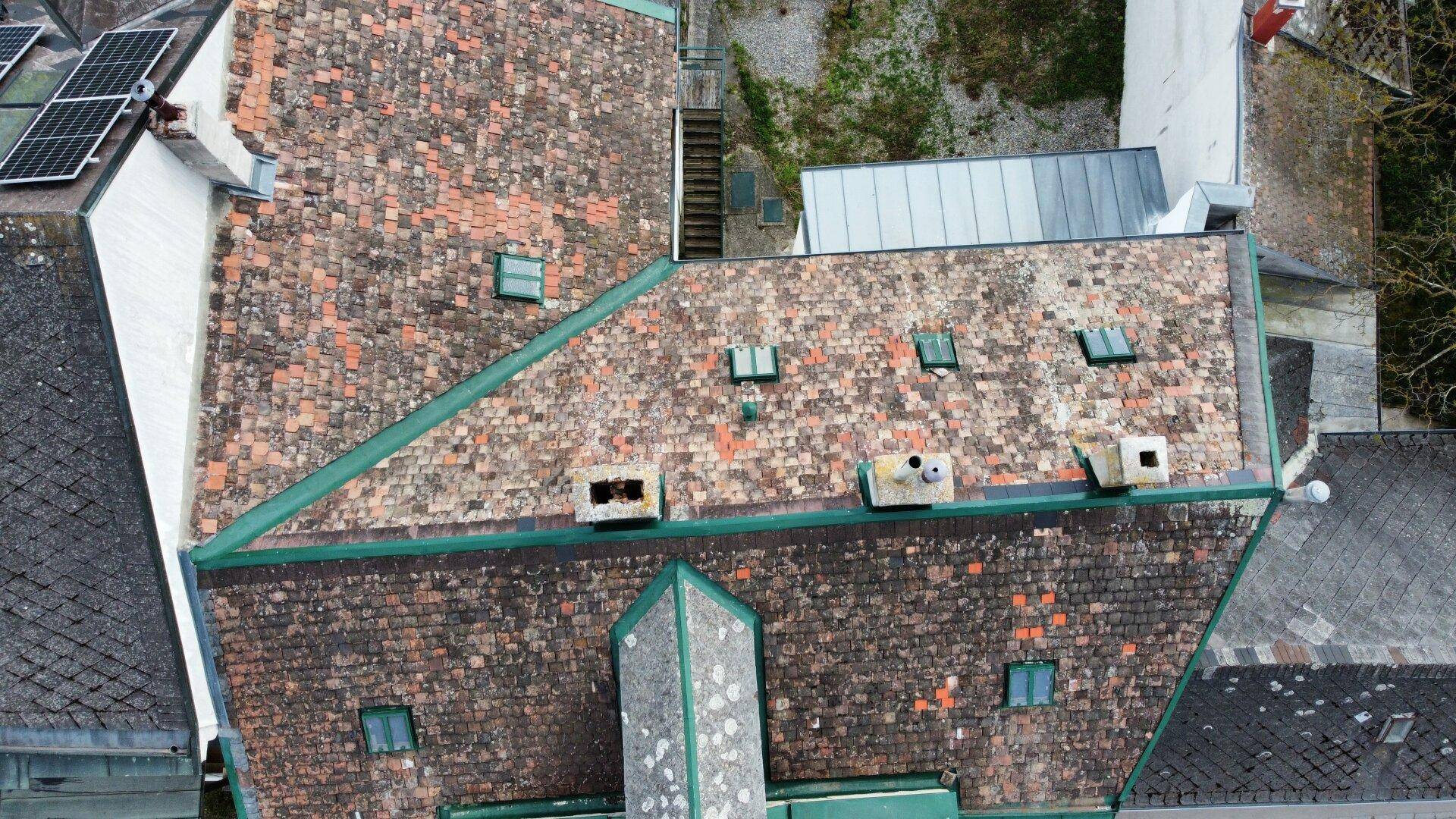 Dachansicht mit alten Ziegeln, Solarpaneelen und mehreren Schornsteinen auf einem Gebäude.