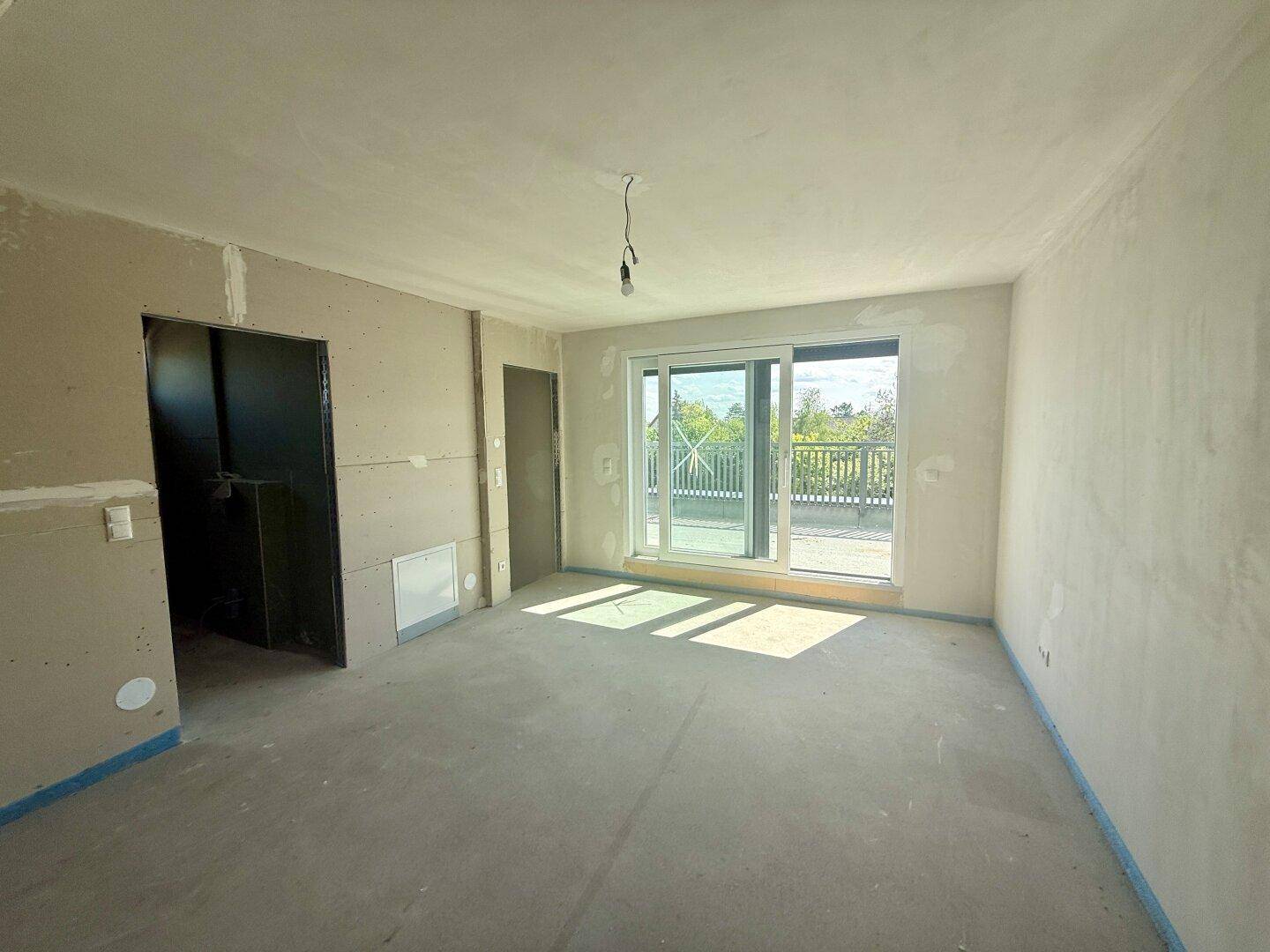 Unfertiger Innenraum mit großen Schiebetüren, die Zugang zu einer Terrasse bieten.