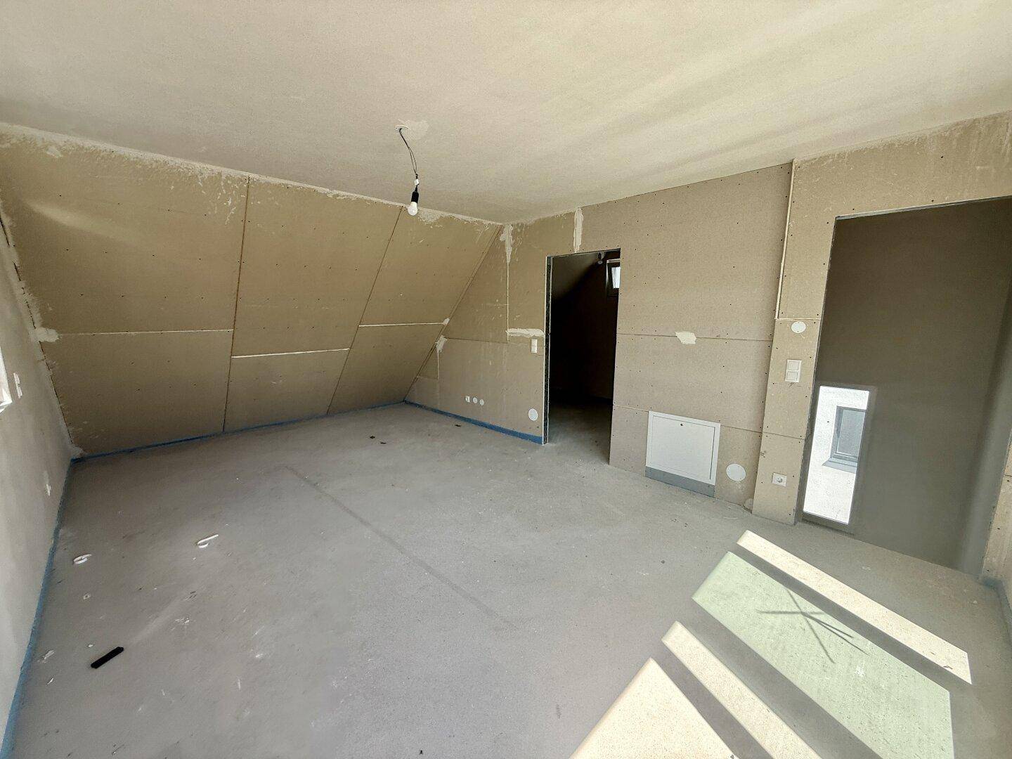 Unfertiges Dachgeschosszimmer mit schräger Decke und Rohbauwänden, bereit für den Ausbau.