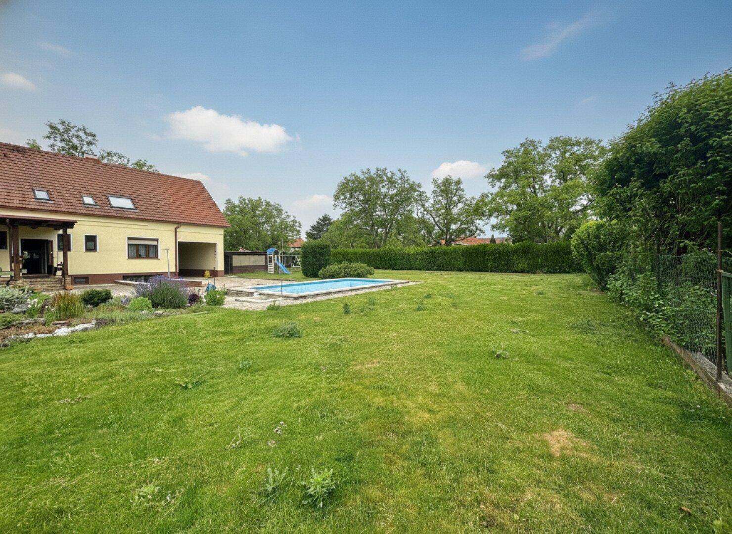 Ausgedehnter Gartenbereich mit Pool, großem Rasen und dem Haus unter blauem Himmel.