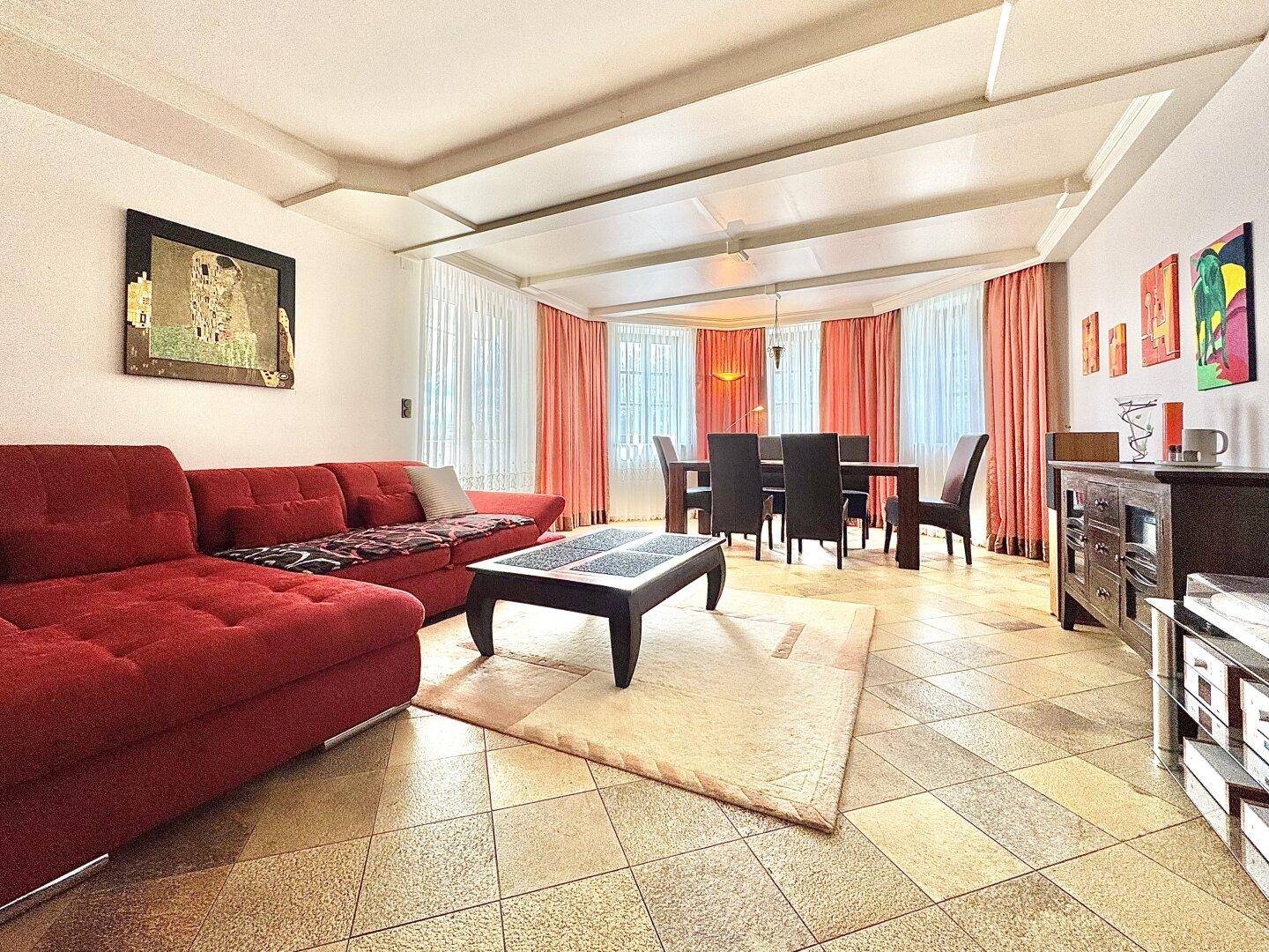 Geräumiger Wohn-Essbereich mit Fliesenboden, rotem Sofa und großem Esstisch.