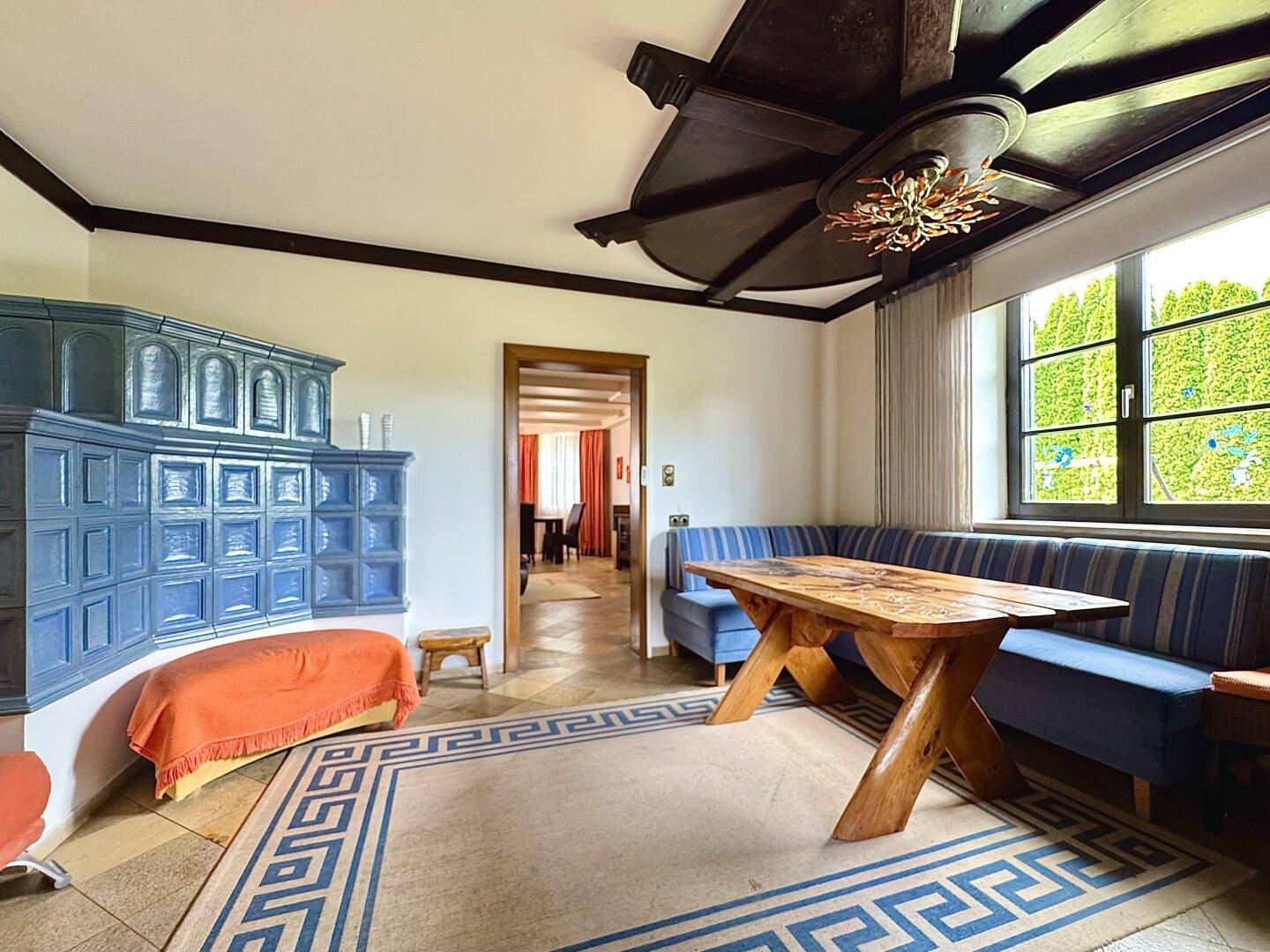 Traditionelles Wohnzimmer mit blauem Kachelofen, Holztisch und Sitzbank.