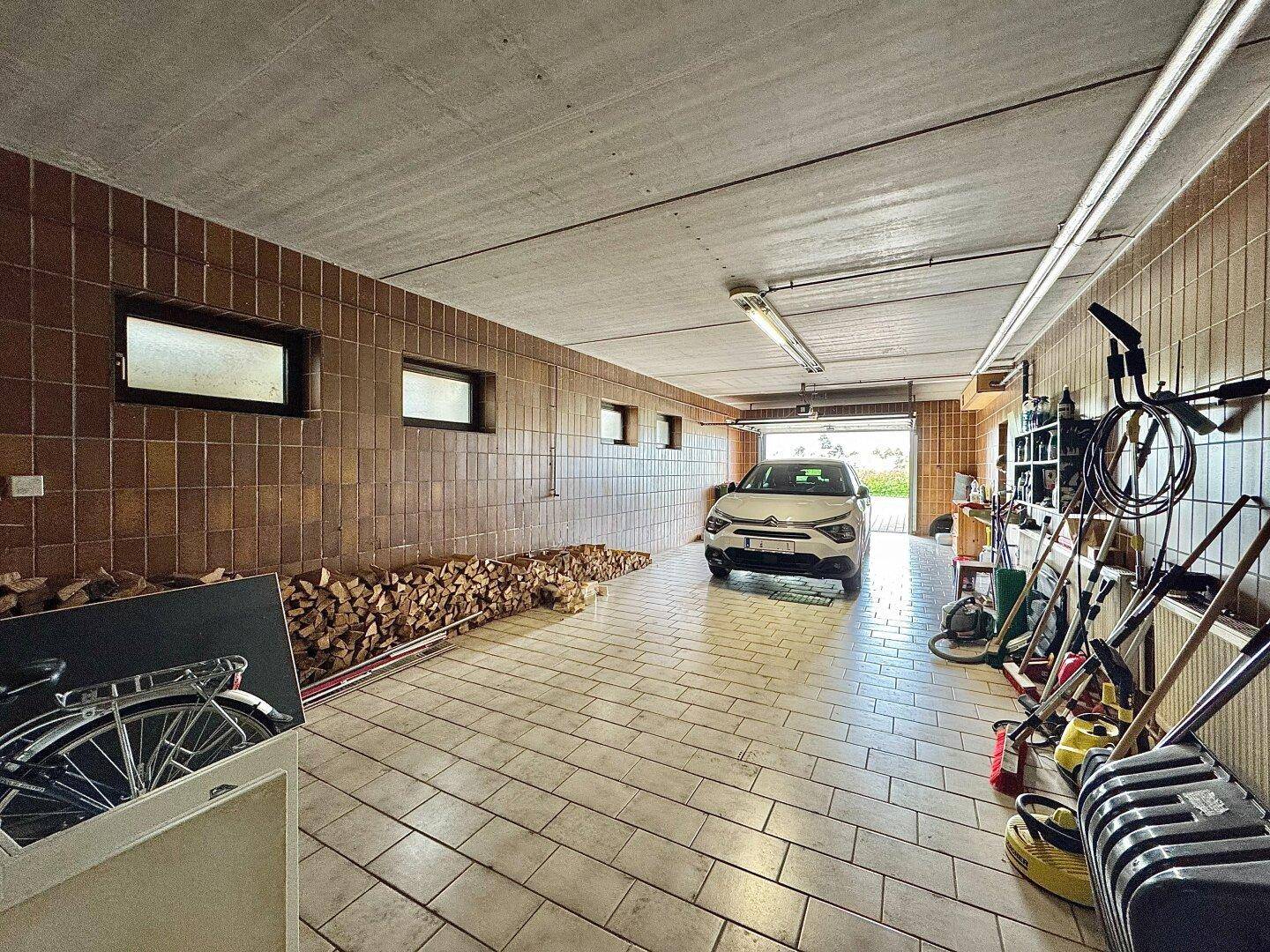 Geräumige Garage mit Fliesenboden, Holzlager und Platz für ein Fahrzeug.